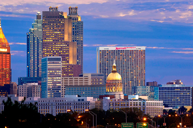 The Atlanta skyline at dusk with the Marriott Marquis sign visible on the upper floors of a large tower. The Georgia State Capitol's gold dome is visible in the foreground.