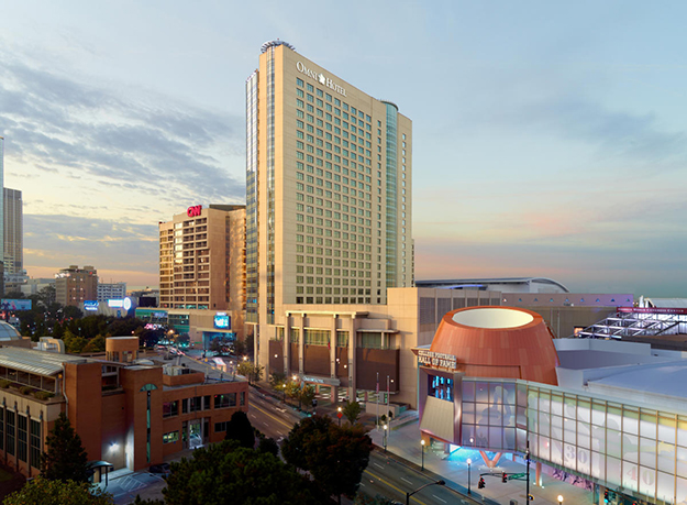 The tall Omni Hotel tower rises above the surrounding downtown Atlanta cityscape at sunset. The CNN Center sign is visible to the left, and the College Football Hall of Fame building appears in the foreground to the right.
